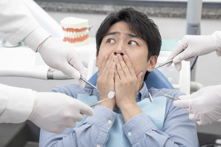 A startled man covering his mouth among hands holding dental instruments