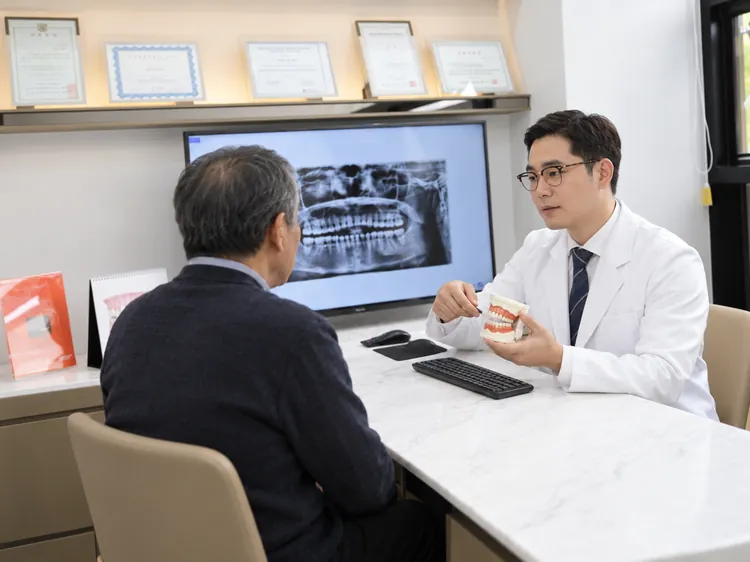 An older patient hearing a dentist explain an X-ray on a monitor